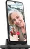 A smartphone is shown in a charging dock, with a video call displayed on the screen. Produktbild-Vorschau