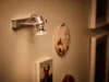A wall with a light fixture and framed art. Anteprima dell’immagine prodotto