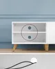 A white media console with wooden legs against a blue wall, with a cable and grommet shown below. Náhled obrázku produktu