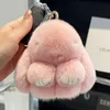 Rosa flauschiger Hasen-Schlüsselanhänger mit weißen Pfoten und goldenen Akzenten, in einer Hand neben einem Autoschlüssel gehalten Anteprima dell’immagine prodotto