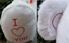 A collage of two close-up images of a white teddy bear. The left image shows the bear's body with red embroidery of 'I ❤️ You'. The right image shows the bear's ear with red stitching detail. Náhľad obrázku produktu