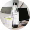 A SodaStream bottle and a glass of water with lemon and mint are on a desk next to a computer monitor. Produktbild-Vorschau