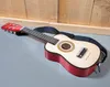 A toy guitar with a strap is lying on a gray surface in front of a wooden wall. Anteprima dell’immagine prodotto