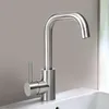 A modern stainless steel faucet is shown in a close-up shot, mounted on a white sink. The background is a plain, light gray wall. Náhled obrázku produktu