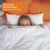 A young girl peeking out from under a white duvet in bed, with orange pillows in the background. Voir les images du produit