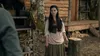 A young woman stands in front of a rustic wooden cabin, looking towards the viewer. The scene appears to be outdoors, possibly in a historical or fantasy setting. Náhľad obrázku produktu