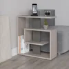 A modern side table with a unique, asymmetrical design, placed next to a sofa. The table has multiple shelves and is decorated with books, a phone, and a small plant. Anteprima dell’immagine prodotto