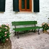 A green wooden garden bench sits on a brick patio in front of a white brick wall with a wooden window and black shutters. Pink flowers are in pots on either side of the bench. Anteprima dell’immagine prodotto
