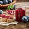 A rustic scene featuring plum jam on bread and a jar of jam, with plums in the background. Voir les images du produit