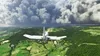 A small white airplane flying over a green landscape towards a runway. Produktbild-Vorschau
