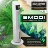 A white tower fan is shown in a natural setting with green plants and water droplets, suggesting a cooling and refreshing experience. Marketing text and logos are overlaid on the image. Voir les images du produit