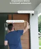 A delivery person is at a wooden door, holding a bag of food. A security camera is mounted on the wall next to the door. Podgląd zdjęcia produktu