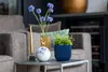 A close-up of decorative items on a side table, including a plant, a vase with flowers, and a candle. Podgląd zdjęcia produktu