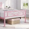 A pink metal bed frame with a decorative headboard is shown in a bedroom setting. Produktbild-Vorschau