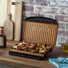 A George Foreman grill with food cooking on it, placed on a wooden countertop with kitchen accessories in the background. Podgląd zdjęcia produktu