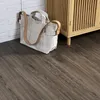 A tote bag rests on a dark brown oak vinyl floor next to a white brick wall and a wooden cabinet. Produktbild-Vorschau