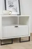 A white bedside table with a fluted drawer front and black metal legs, shown in a room setting with a framed picture and a cup on top. Podgląd zdjęcia produktu