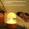 A woman sleeping in bed next to a mushroom-shaped humidifier that is emitting mist and light. Náhled obrázku produktu