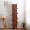A tall, narrow bookshelf with a tree-like design stands against a white wall. To the left, a wooden table with a clock and a small plant is visible. Podgląd zdjęcia produktu