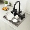 A kitchen sink with a faucet running water into it, dishes are being washed and drying on a rack. Náhled obrázku produktu