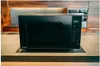 A black Panasonic microwave oven with a digital display is placed on a wooden countertop in a modern kitchen. Anteprima dell’immagine prodotto