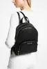 A woman wearing a white sweater and white pants is shown from the back, wearing a black Michael Kors backpack. Produktbild-Vorschau