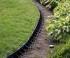 A garden border made of black plastic is installed between a lawn and a garden bed with plants. Produktbild-Vorschau