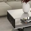 A close-up view of a modern coffee table with a white top and black marble-patterned sides, placed in a living room setting next to a sofa. Anteprima dell’immagine prodotto