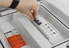 A hand is shown inserting a blue fuse into a white electrical component within a gray enclosure. Náhled obrázku produktu