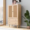 A wooden cabinet with cane doors and drawers, placed next to a window with a view of buildings and a large potted plant. Produktbild-Vorschau