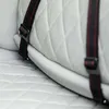 A close-up view of a white quilted seat with black and red straps attached. Produktbild-Vorschau