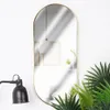 A mirror with a gold frame is shown against a white wall, with a black lamp and green plants. Produktbild-Vorschau