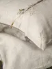 A close-up of a textured fabric, likely bedding, with a sprig of dried grass resting on it. A small grey tag with the brand name is visible. Produktbild-Vorschau