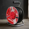 A heavy-duty extension cord reel with a black cable, red outlets, and a silver metal stand, set against a dark gray background. Produktbild-Vorschau