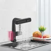 A black kitchen faucet with a digital display is shown running water into a sink. There are also some baked goods and cherries on a cutting board in the background. Náhled obrázku produktu