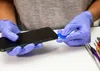 Hands wearing blue gloves are shown disassembling a black smartphone with a blue plastic tool. Produktbild-Vorschau