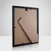 The back of a black picture frame with a stand, displayed on a reflective surface against a light gray background. Anteprima dell’immagine prodotto