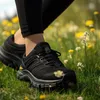 A person wearing black leggings and black Salomon shoes walks through a field of green grass and yellow wildflowers. Náhled obrázku produktu