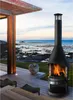 A modern outdoor fireplace on a wooden deck overlooking the ocean at sunset. Produktbild-Vorschau
