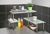 A kitchen counter with a multi-tiered stainless steel shelf unit holding various kitchen items. Anteprima dell’immagine prodotto