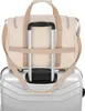 A beige duffel bag is placed on top of a silver rolling suitcase, with the handles of both visible. Náhled obrázku produktu