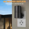 A black LED night light plugged into a white wall socket, with a hint of an outdoor sauna in the background. Produktbild-Vorschau
