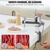 A close-up of a manual meat grinder with a hand turning the crank, surrounded by chopped meat and different grinding plates. Náhľad obrázku produktu