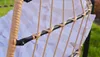 Close-up view of the woven structure of a hanging chair, showing the natural fiber weaving around a black metal frame, with a striped cushion visible in the background. Podgląd zdjęcia produktu