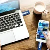 A person is using a USB stick to transfer data between a smartphone and a laptop, with a cup of coffee nearby. Náhľad obrázku produktu