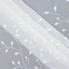 A close-up view of white sheer fabric with embroidered leaf patterns, folded and layered. Produktbild-Vorschau