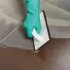 A gloved hand is using a trowel to apply grout to tile. Produktbild-Vorschau
