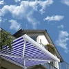 A retractable awning with blue and white stripes is extended from a house under a blue sky with white clouds. Produktbild-Vorschau