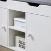 Close-up view of a white storage bench with a gray upholstered top, showing two open compartments with boxes inside. Produktbild-Vorschau