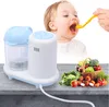 A baby being fed with a spoon next to a baby food maker and a basket of fresh vegetables. Produktbild-Vorschau